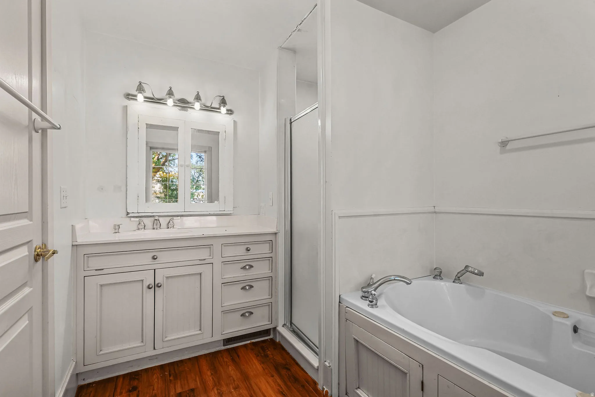 Built-in vanity with a white countertop and undermount sink, wood-finish flooring, built-in medicine cabinet with mirrored doors, and a built-in tub