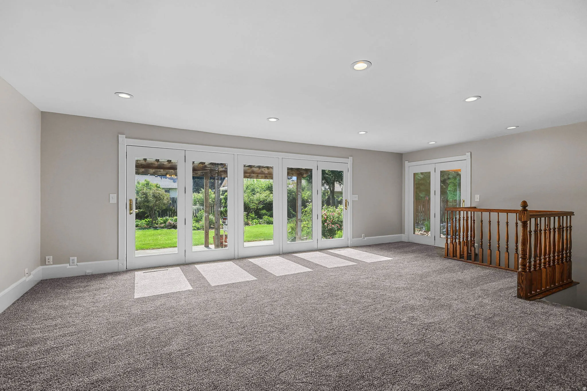 Recessed ceiling lighting, gray carpeting, a multi-panel glass door, a double-panel glass door, and a wood railing
