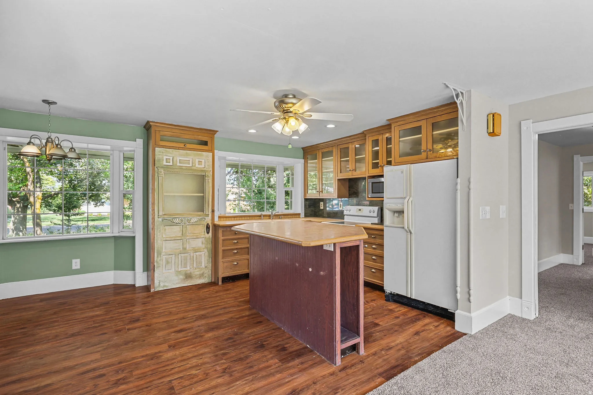 Wood-finish flooring with a ceiling fan, wood cabinetry with glass fronts, and a kitchen island