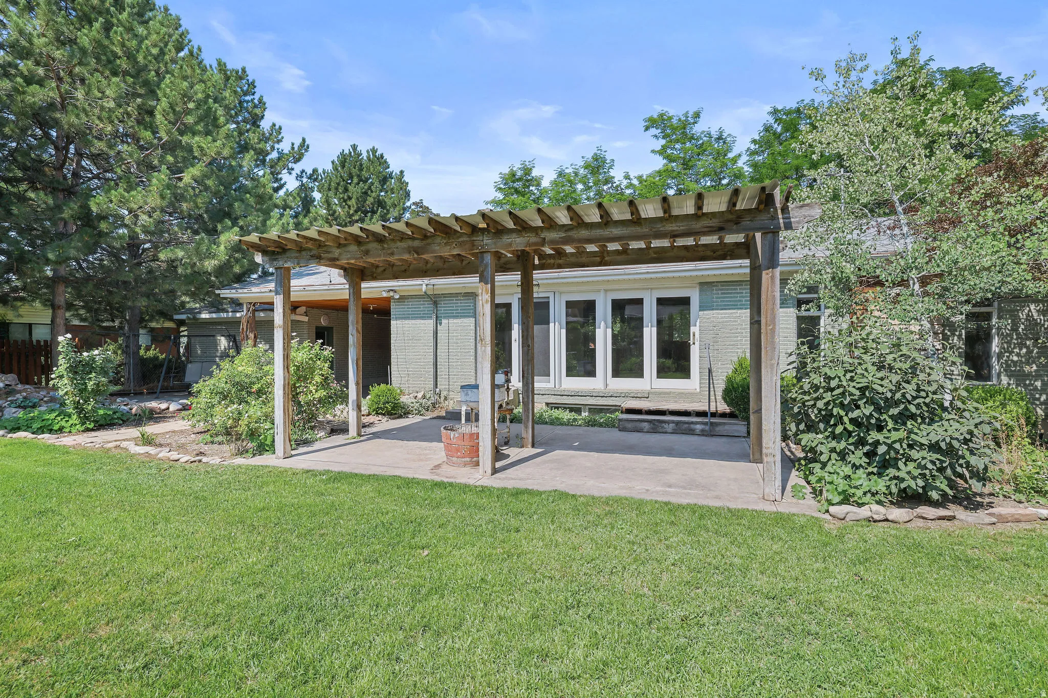 Expansive lawn area with a concrete patio featuring a wood pergola