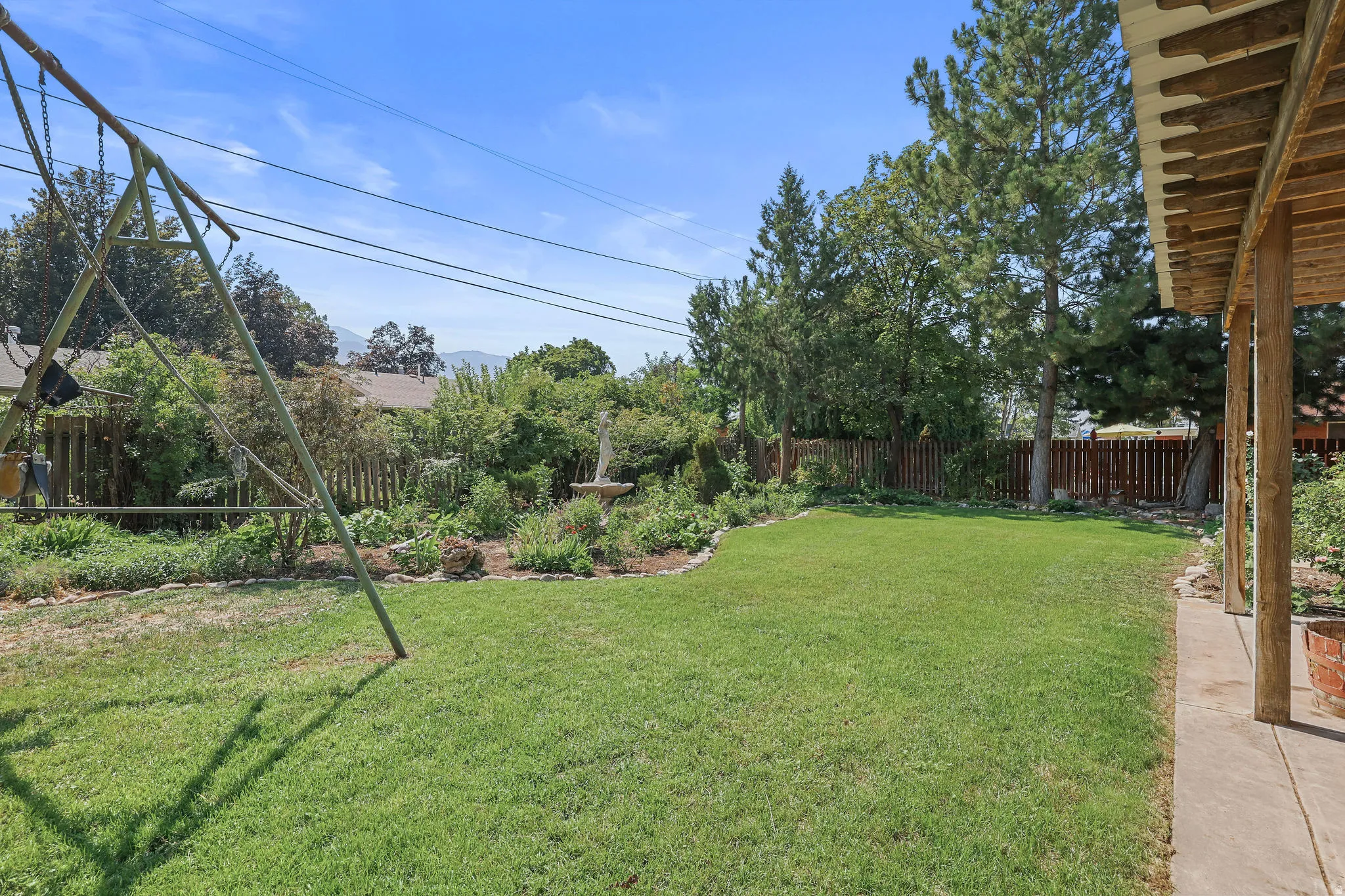 Expansive grassy yard with mature landscaping, a privacy fence, and an attached covered patio