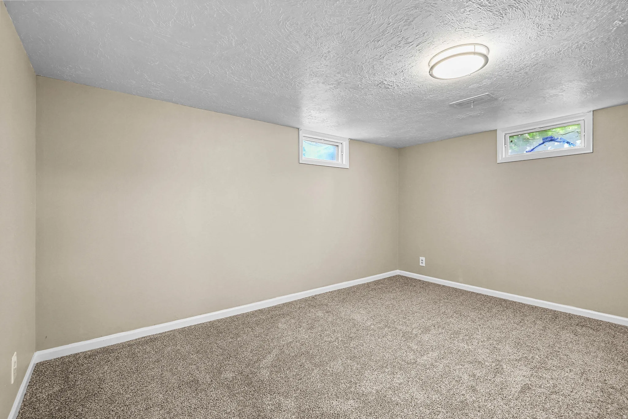 Neutral tone wall paint, textured ceiling, two horizontal windows, recessed ceiling light fixture, and carpeted flooring