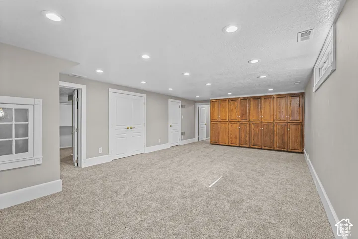 Recessed lighting, plush carpet flooring, wood-finish cabinetry, white trim, and a window well