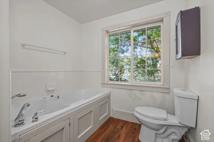 Built-in soaking tub with paneling, wood-finish flooring, and a large window with grilles