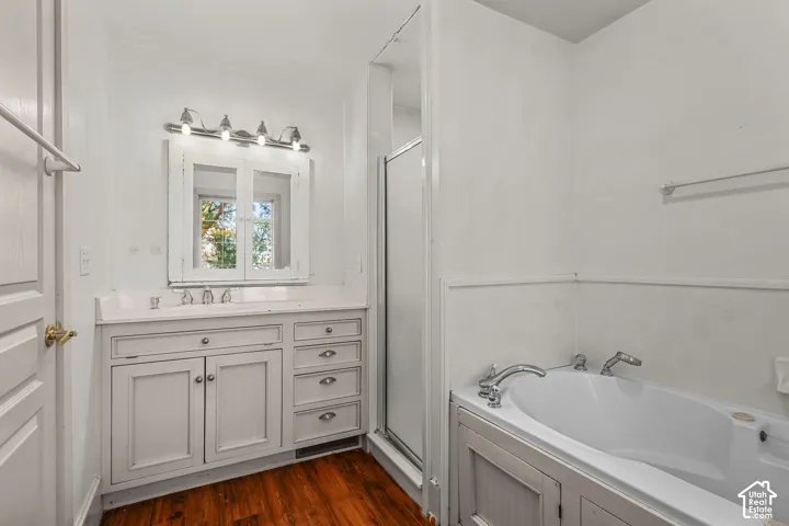 Built-in vanity with a white countertop and undermount sink, wood-finish flooring, built-in medicine cabinet with mirrored doors, and a built-in tub