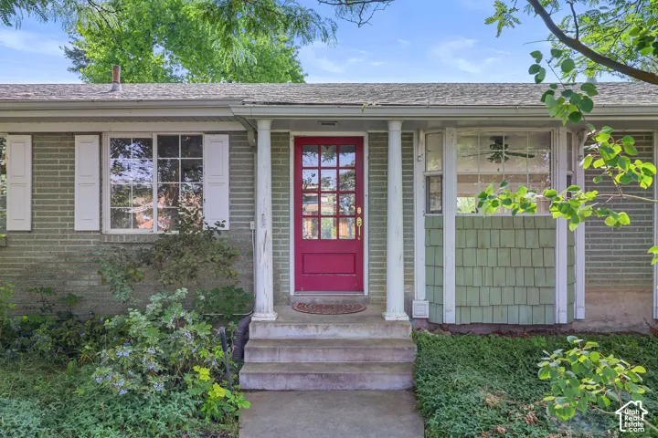 Brick exterior with a distinctive red front door, prominent white columns, and a bay window featuring green shaker siding