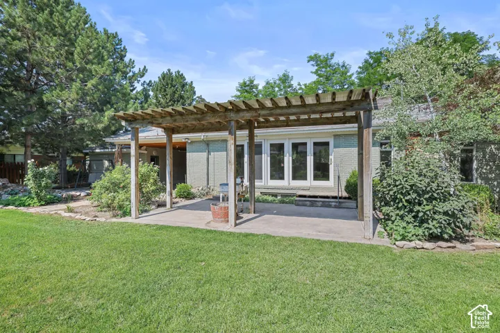 Expansive lawn area with a concrete patio featuring a wood pergola