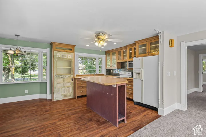 Wood-finish flooring with a ceiling fan, wood cabinetry with glass fronts, and a kitchen island
