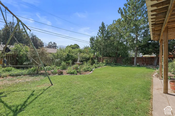 Expansive grassy yard with mature landscaping, a privacy fence, and an attached covered patio