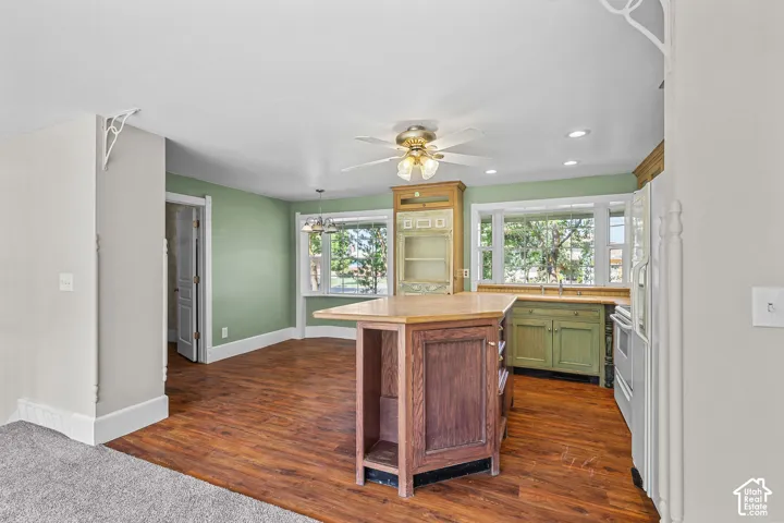 Wood-finish flooring, central kitchen island with countertop, recessed lighting, ceiling fan, and bay windows