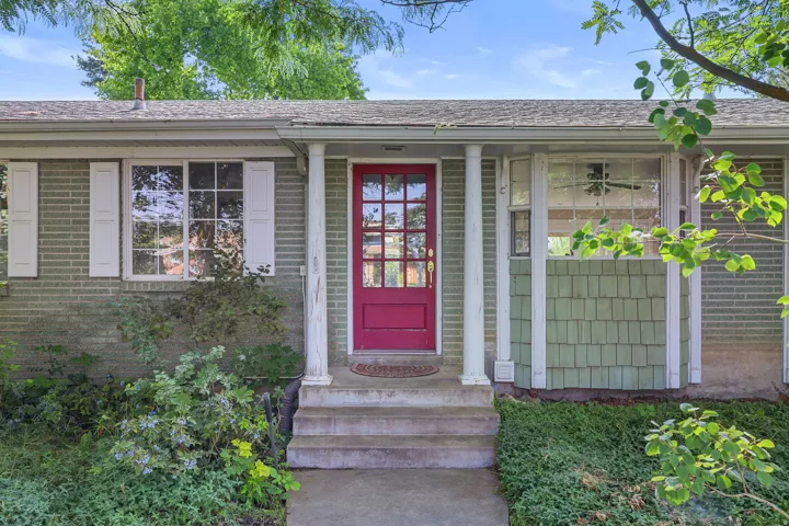 Brick exterior with a distinctive red front door, prominent white columns, and a bay window featuring green shaker siding