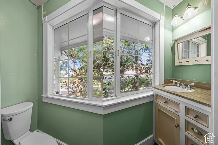 Bay window with white framing, built-in vanity with a single basin sink, wall-mounted light fixture, and a framed mirror
