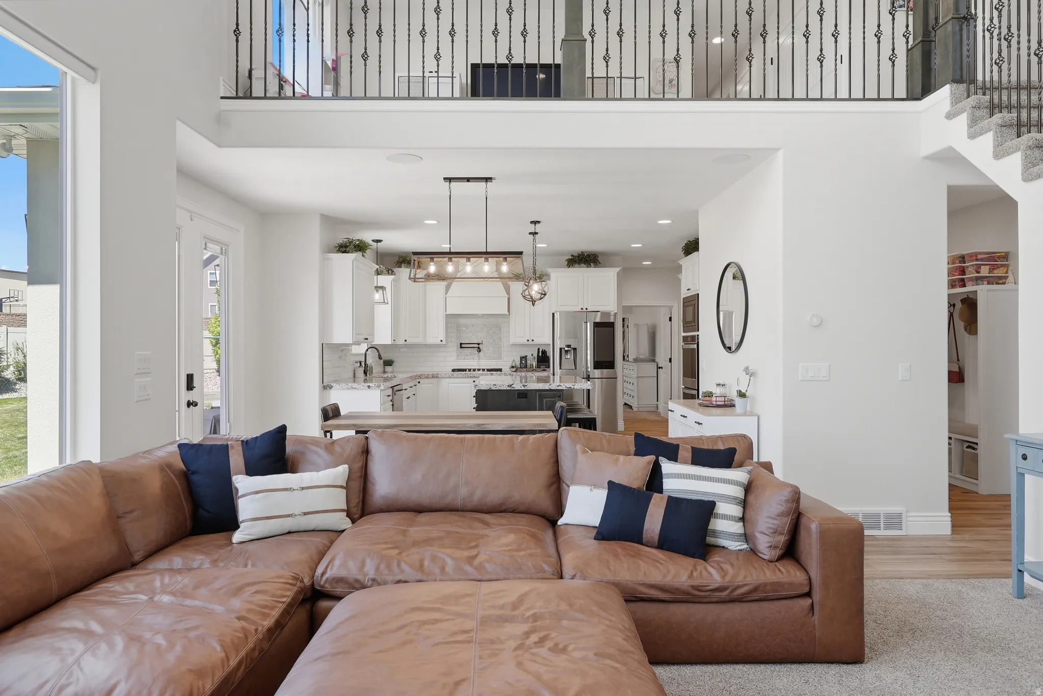 Open concept design with a two-story ceiling, kitchen featuring white cabinetry, and an upper-level balcony with wrought iron balusters