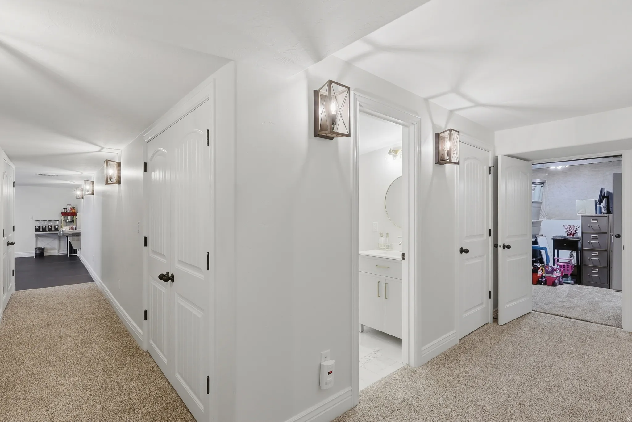 Carpeted hallway with white walls, multiple paneled doors, and wall-mounted light fixtures