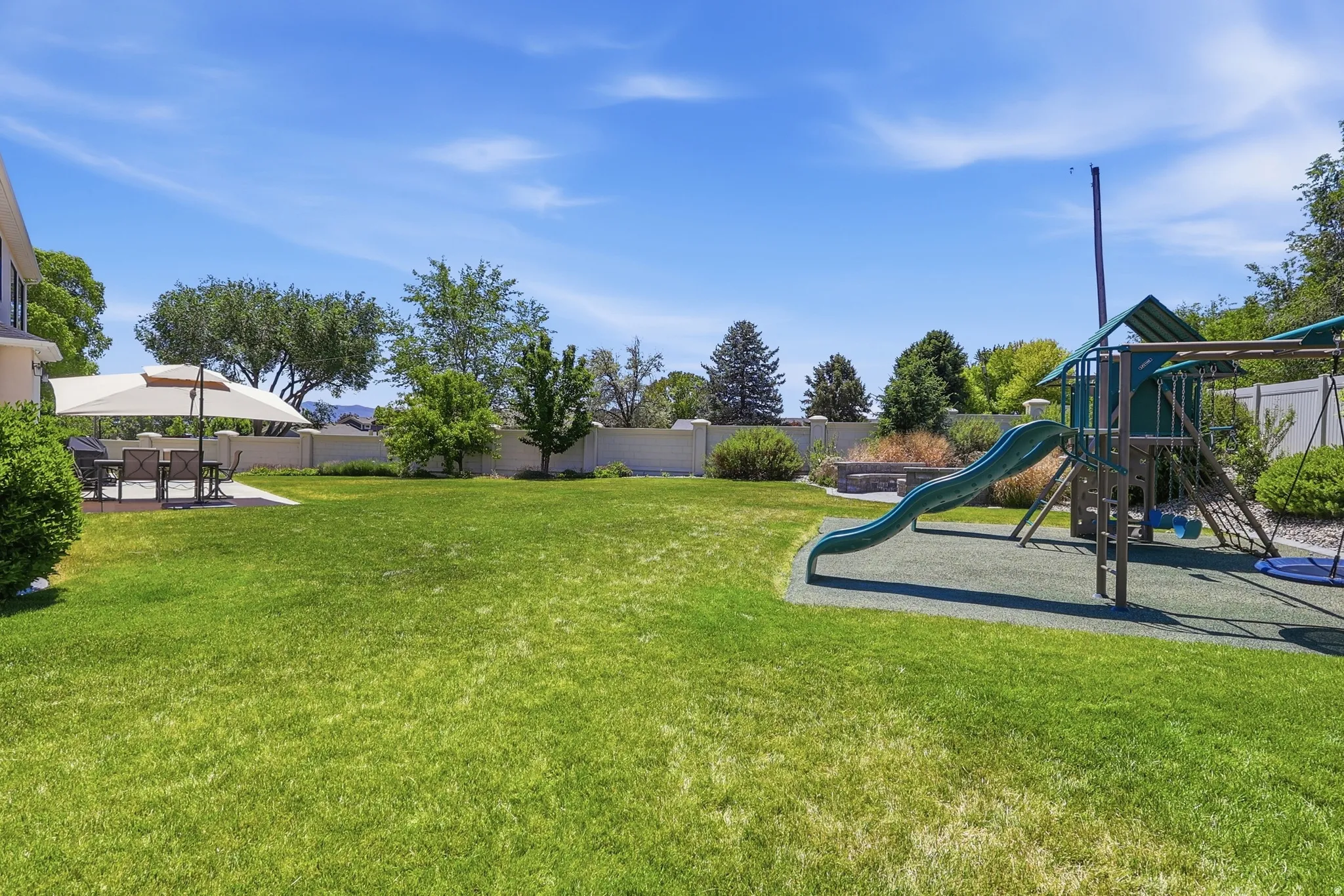 Expansive lawn area with a built-in play structure, paved patio, and mature landscaping