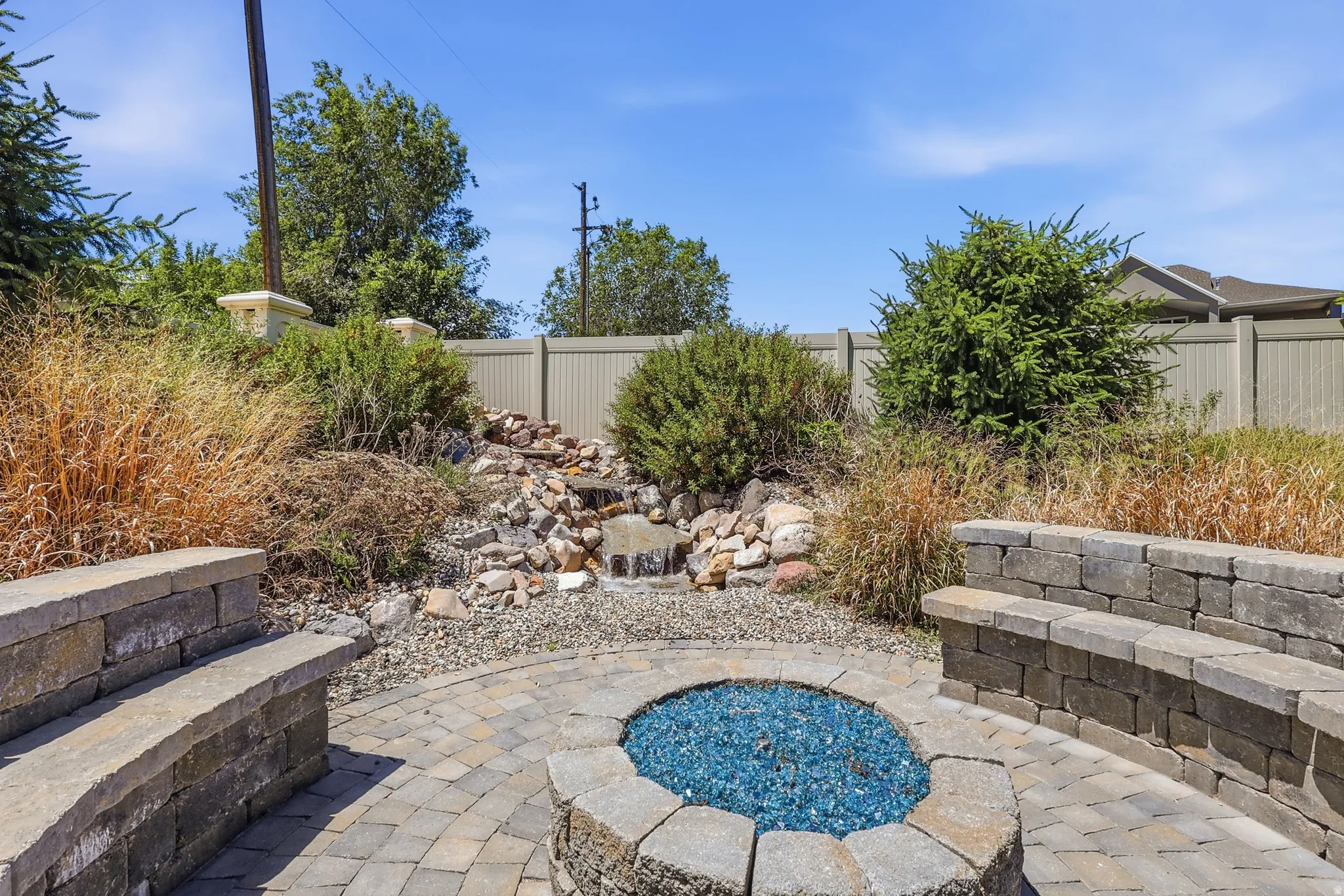 Paver patio with a built-in stone gas fire pit, integrated stone seating, and an app controlled rock waterfall feature