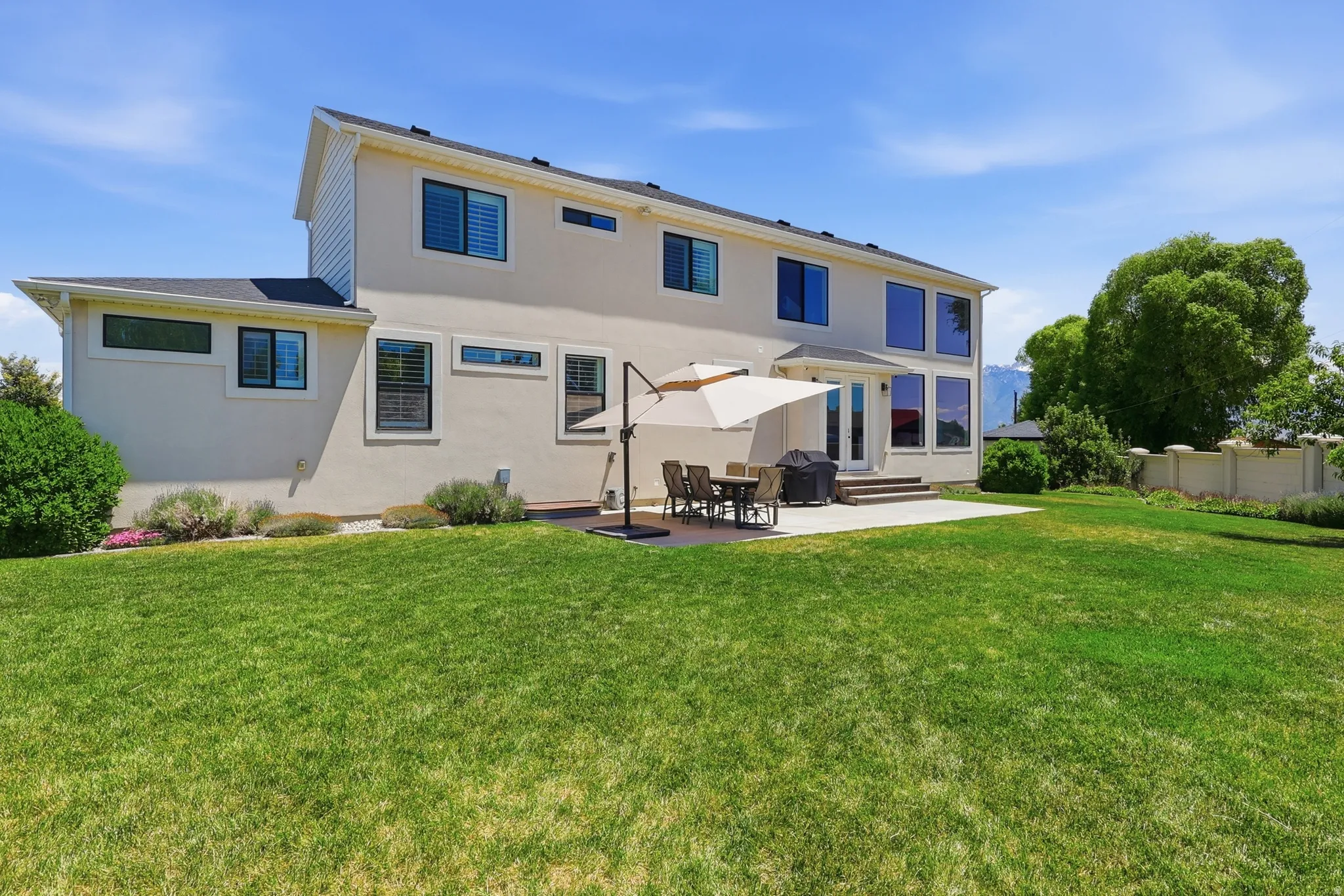 Expansive green lawn, stucco exterior, multiple large windows, ground-level Trex deck, patio, and a privacy wall