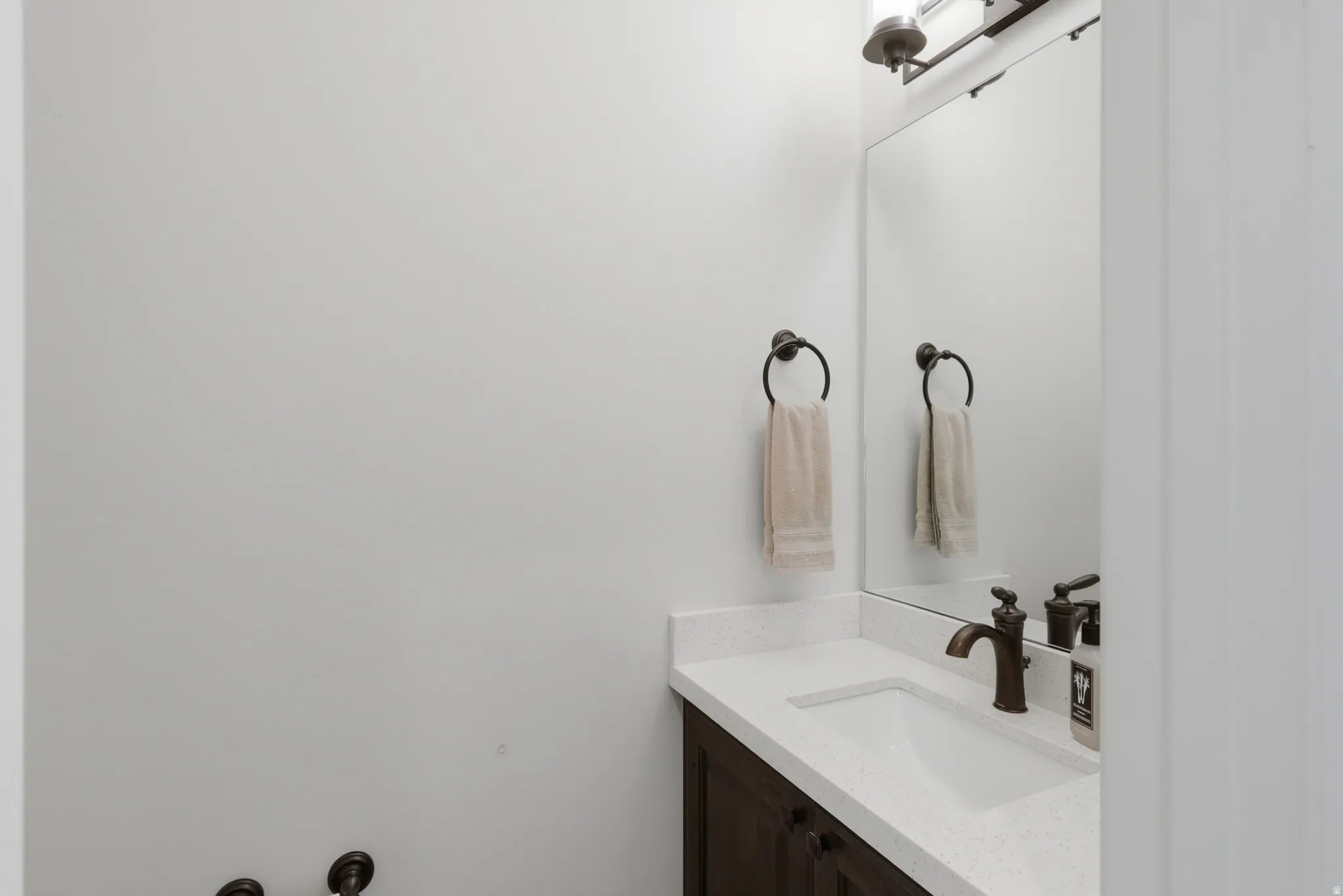 Powder room featuring a dark wood vanity, white countertop, integrated sink, and bronze faucet