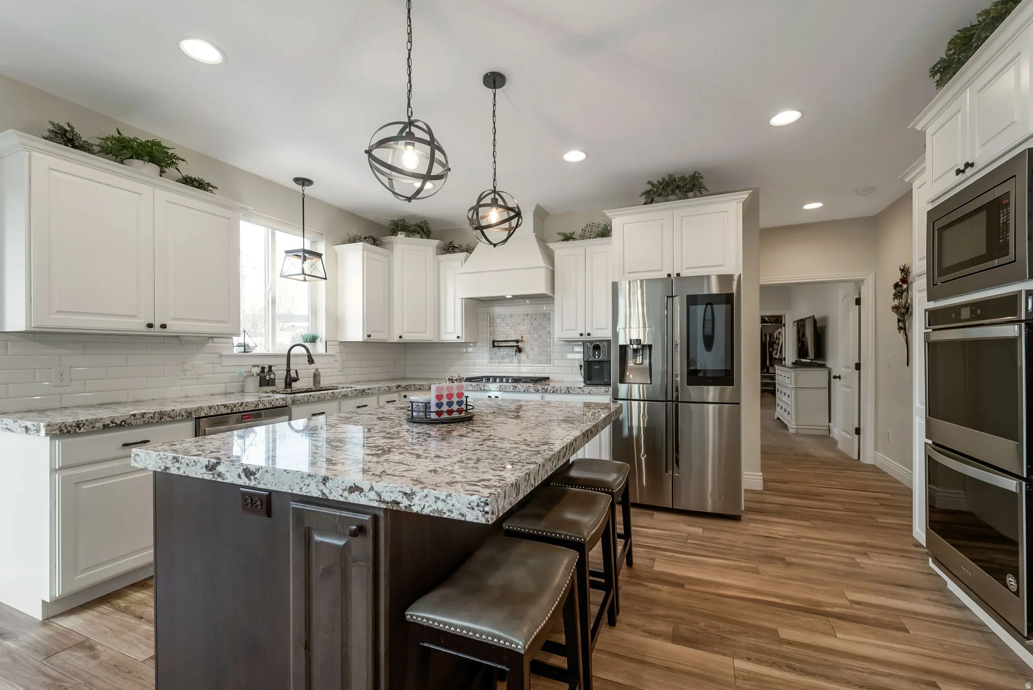 Spacious kitchen featuring an expansive island, white cabinetry, integrated stainless steel appliances, wood-finish flooring, and pendant lighting