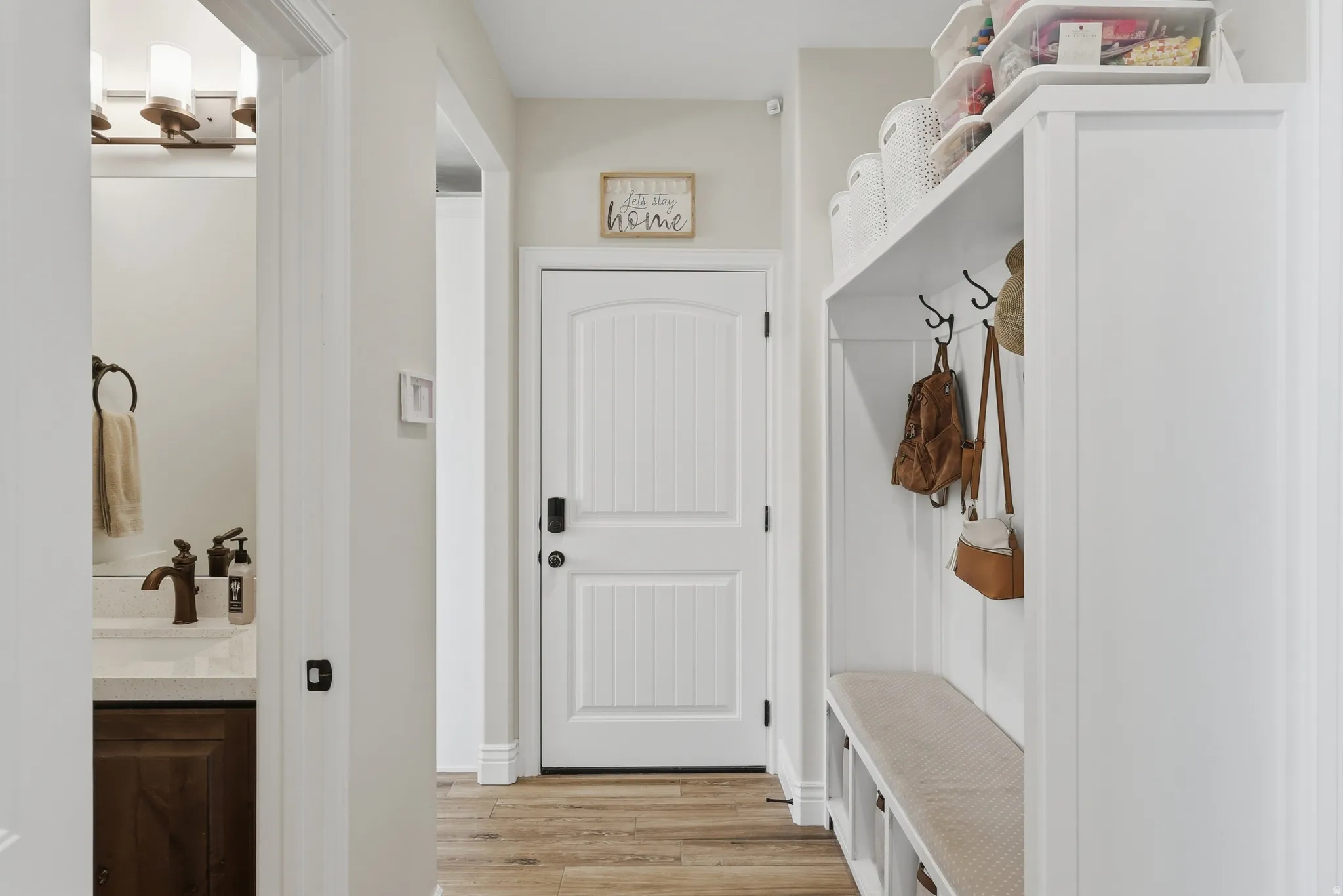 Hallway featuring wood-finish flooring, a white paneled door, and a built-in storage bench with coat hooks