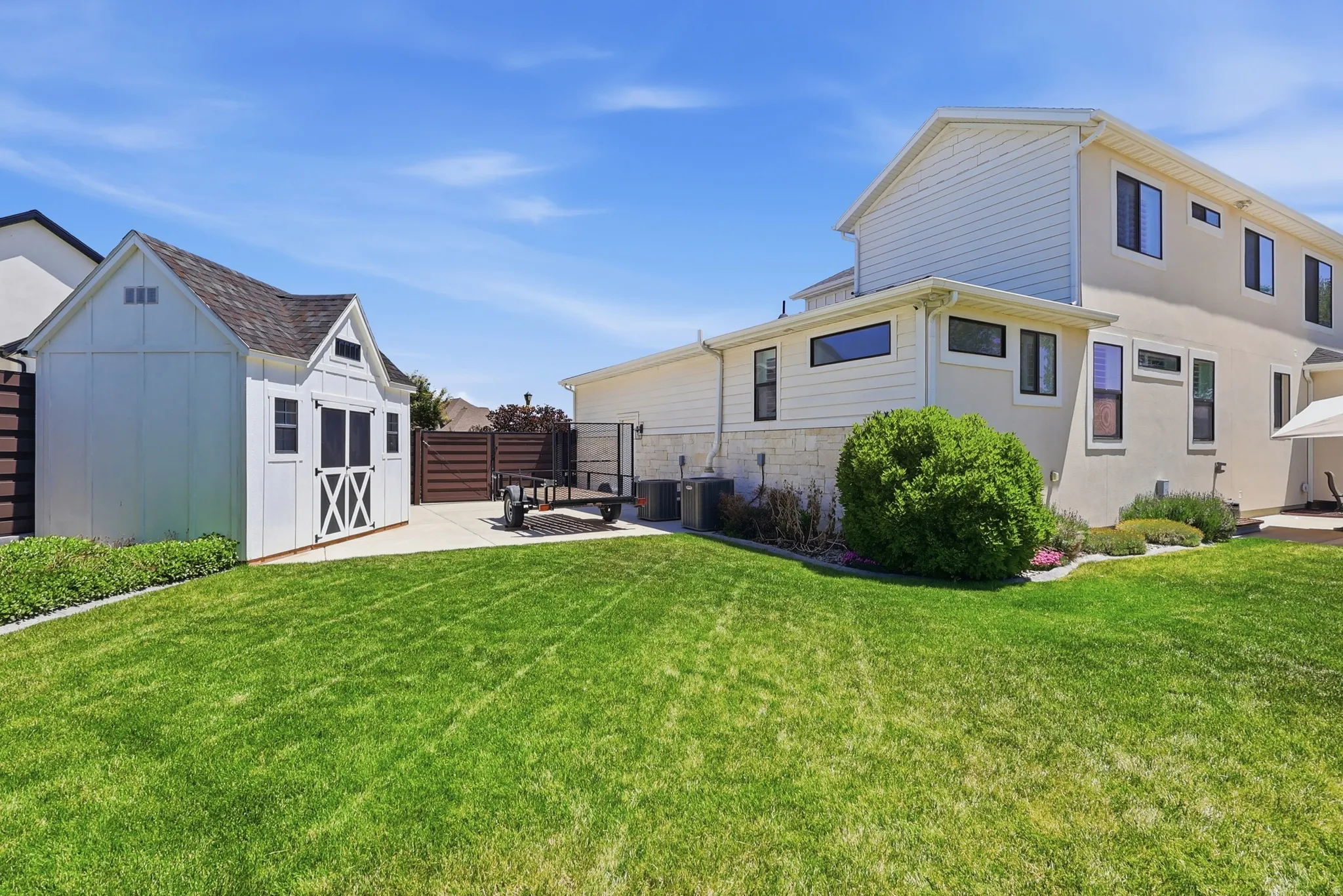 Expansive green lawn with a white storage shed and concrete patio