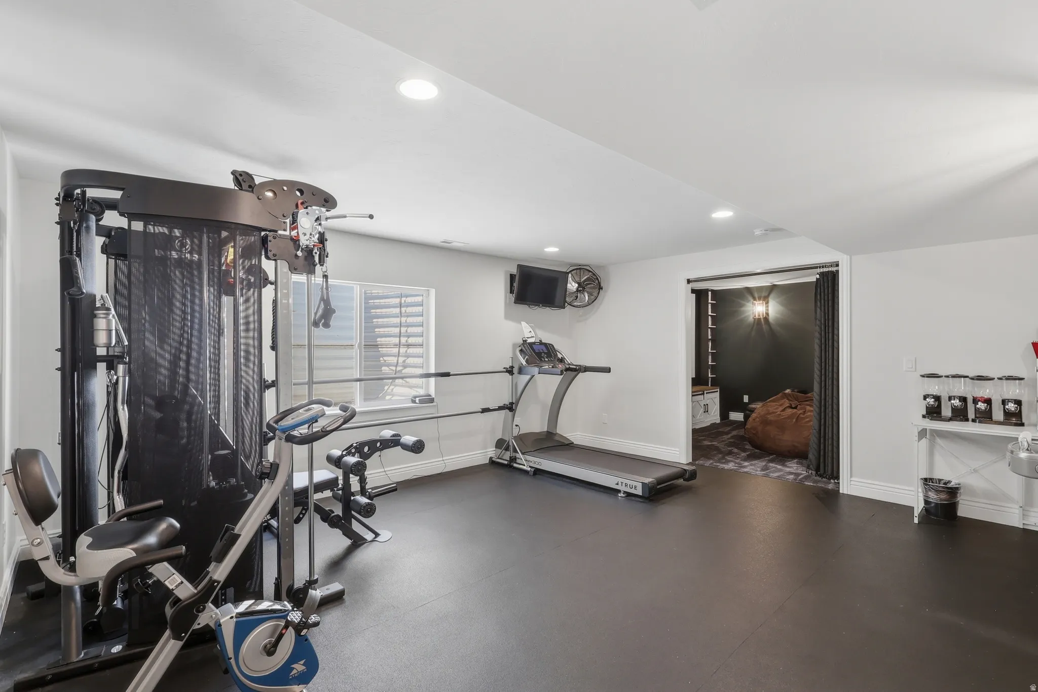 Spacious recreation room featuring recessed lighting, a window with horizontal blinds, and dark flooring