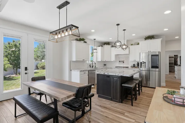 Open-concept kitchen with wood-finish flooring, white cabinetry, a dark-toned kitchen island with a light-toned countertop, and stainless steel appliances