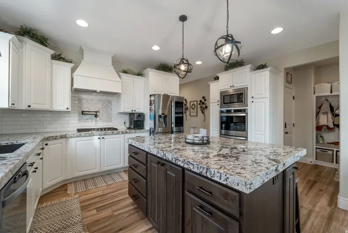 Kitchen featuring a large island with a stone countertop, white shaker-style cabinetry, wood-finish flooring, a built-in oven and microwave, and globe pendant lighting