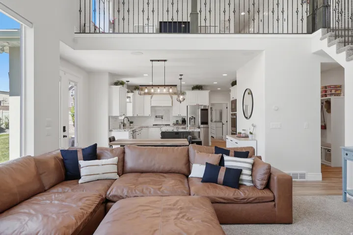 Open concept design with a two-story ceiling, kitchen featuring white cabinetry, and an upper-level balcony with wrought iron balusters