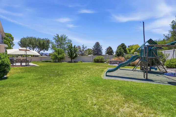 Expansive lawn area with a built-in play structure, paved patio, and mature landscaping