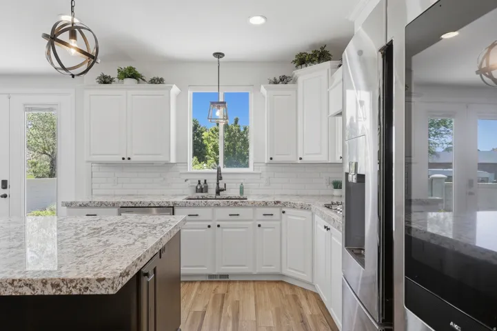 White cabinetry with dark hardware, stone countertops, stainless steel appliances, subway tile backsplash, and wood-finish flooring