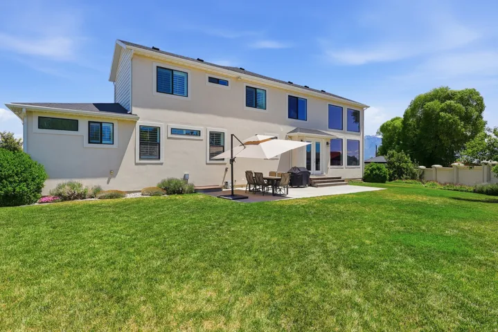 Expansive green lawn, stucco exterior, multiple large windows, ground-level Trex deck, patio, and a privacy wall