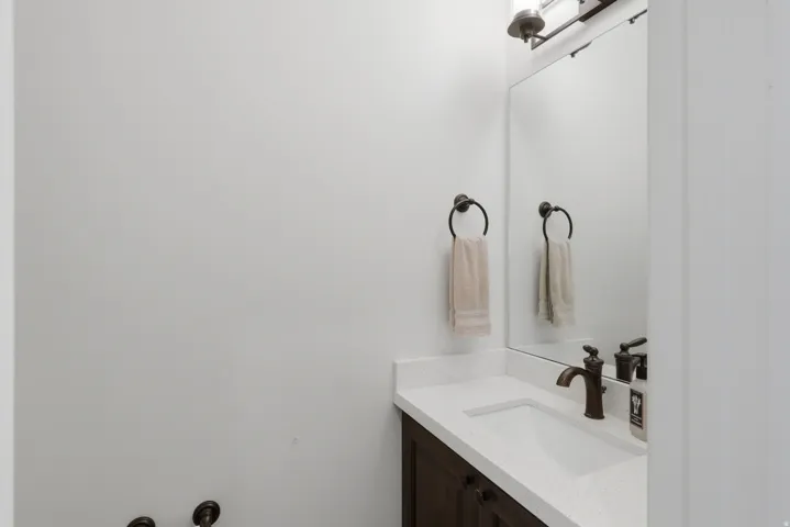 Powder room featuring a dark wood vanity, white countertop, integrated sink, and bronze faucet