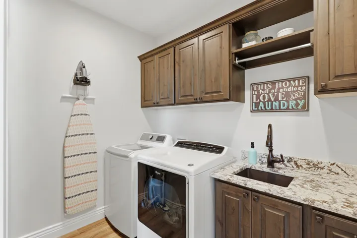 Wood-finish flooring, built-in upper cabinetry, granite-finish countertop, undermount sink, and wall-mounted drying rod
