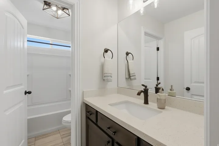 White vanity with a single basin, light-toned countertop, and bronze-finish faucet