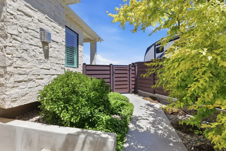 Stacked stone exterior, concrete pathway, lush shrubbery, privacy fencing, side gate access