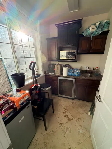 Kitchenette featuring dark wood-finish cabinetry, a built-in microwave, a stainless steel beverage refrigerator, a sink with dark countertops, and large paneled windows