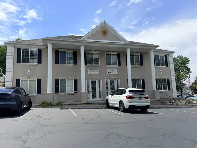 Two-story commercial building with a light-colored stucco exterior, prominent white columns, and dark window shutters