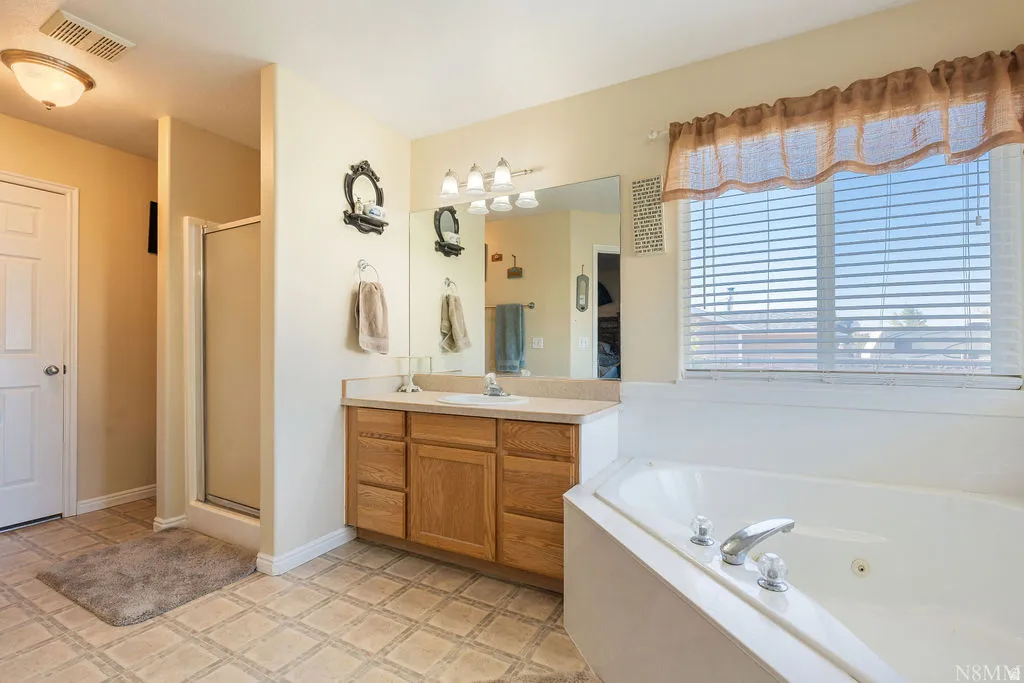 Spa-inspired primary bathroom featuring a wood-finish vanity with dual sinks, engineered stone countertop, and large framed mirror with integrated lighting