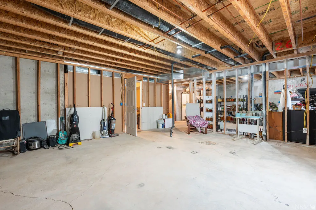 Unfinished basement featuring exposed wood joists, concrete foundation walls, and framed interior walls