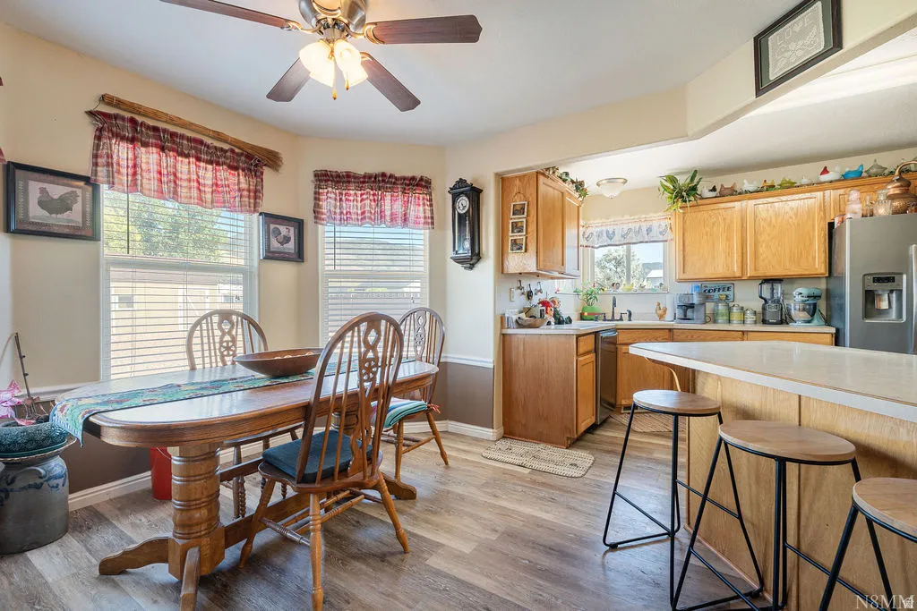 Open-concept kitchen and dining area featuring wood cabinetry with stainless steel appliances, wood-finish flooring throughout, and a breakfast bar with seating