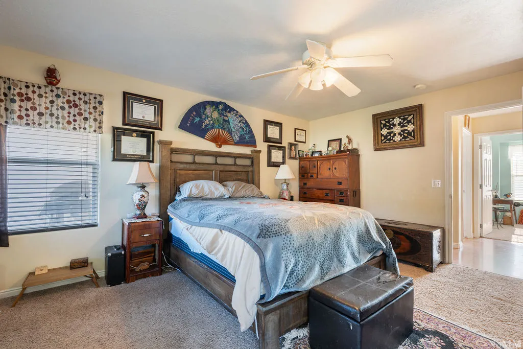 Ceiling fan with integrated lighting, window with blinds, carpeted flooring, wood-finish bed frame, and a doorway