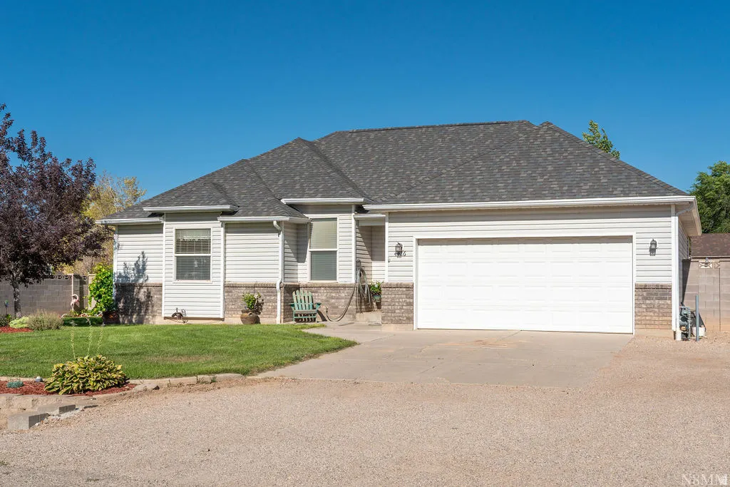 Welcoming ranch-style home featuring a two-car attached garage, brick and vinyl exterior, pitched roofline with architectural shingles, front entry with covered porch, and manicured landscaping with mature trees and defined garden beds