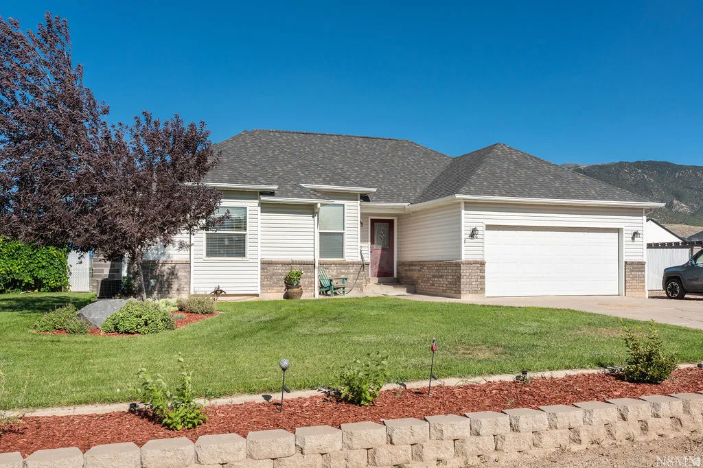 Charming single-story home featuring cream-colored vinyl siding, a dark-pitched roof with composite shingles, and a two-car attached garage