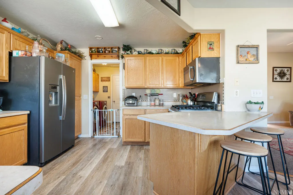 Kitchen featuring wood-finish flooring, light wood cabinetry, stainless steel appliances, and a central island with counter seating
