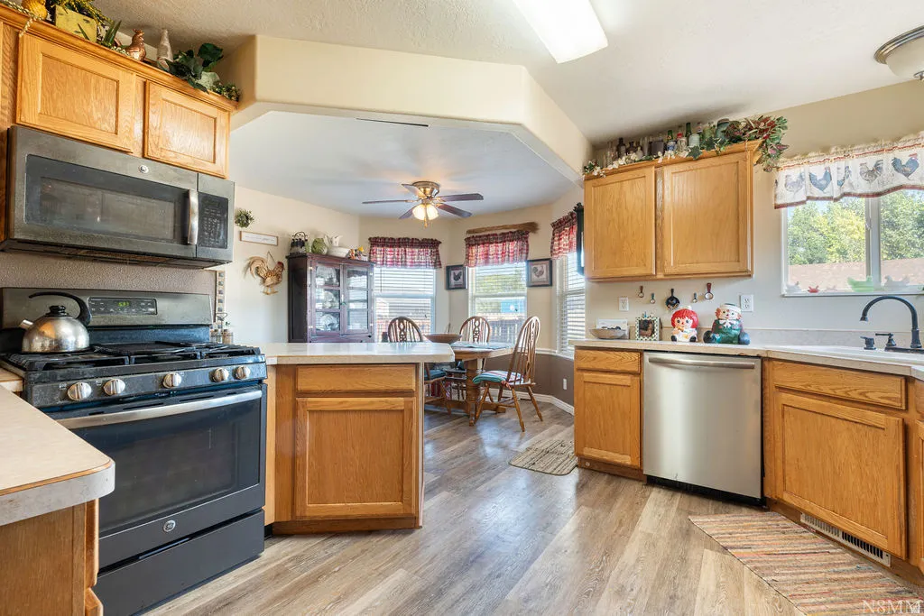 Wood-finish flooring, light wood cabinetry, white countertops, built-in microwave, and stainless steel dishwasher