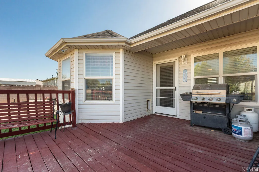Expansive red-stained deck with a matching wood railing, featuring light-colored horizontal siding, multiple windows, and a screened door