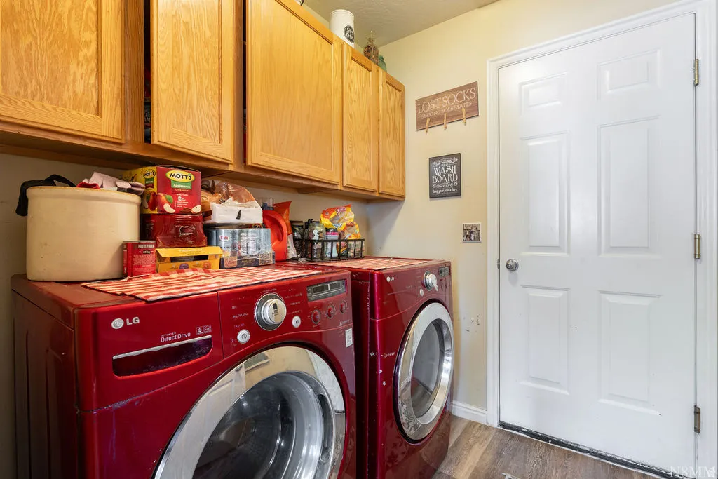 Dedicated laundry room featuring side-by-side front-load LG washers and dryers in bold red finish, wood-finish cabinetry with ample storage above, and wood-finish flooring throughout
