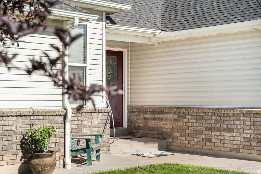 Welcoming front entry featuring a brick and siding exterior with contrasting materials, a solid wood entry door with decorative glass paneling, and manicured landscaping with established plantings