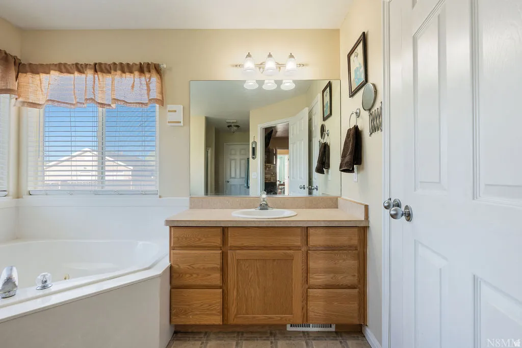 Master bathroom featuring a wood-finish vanity with dual-sink configuration, marble-look countertop, and three-light fixture above the mirror